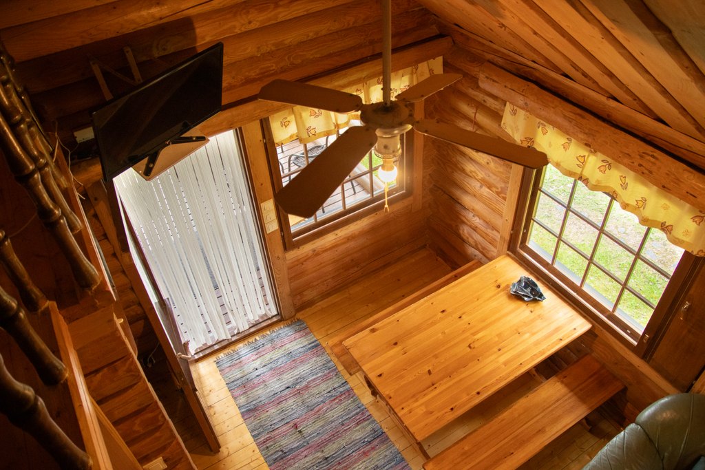 Kankijärven mökin sisätilaa kuvattuna parvelta. Seinällä televisio ja alhaalla pirtinpöytä.