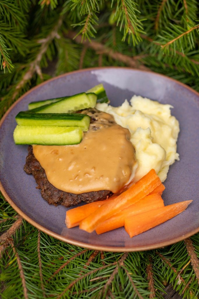 Pieni jauhelihapihvi, jonka päällä kastiketta. Vieressä perunamuusia sekä kurkku- ja porkkanatikkuja.