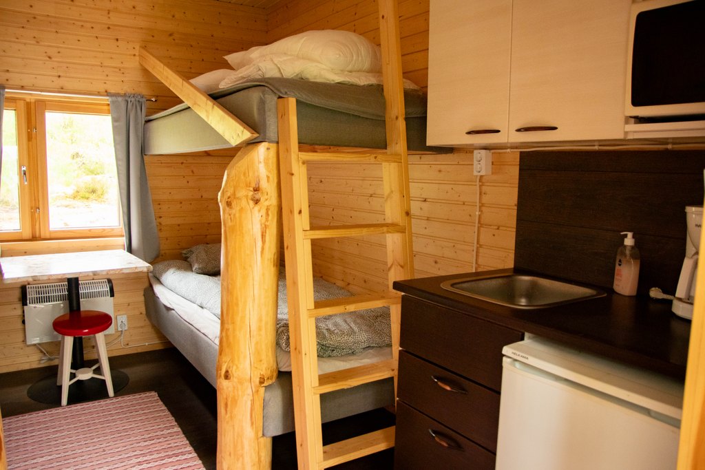 Portinvartijat 1, 2 ja 3 Portinvartija-mökin sisätilaa, jossa kelopuista rakennettu kerrossänky ja pieni keittiönurkkaus.
