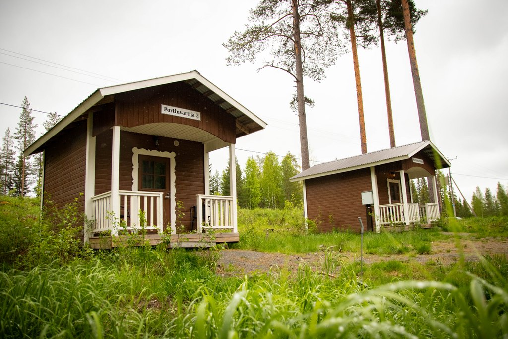 Portinvartijat 1, 2 ja 3 Portinvartija 1- ja Portinvartija 2-mökit kuvattuna pilvisenä kesäpäivänä. Mökit seisovat vierekkäin parkkialueen vieressä.