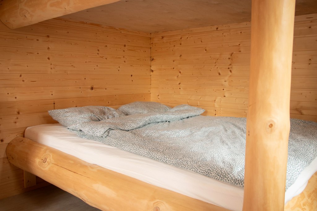 Portinvartijat 1, 2 ja 3 Kelopuista rakennetun kerrossängyn alempi sänky, jossa sinertävät lakanat.